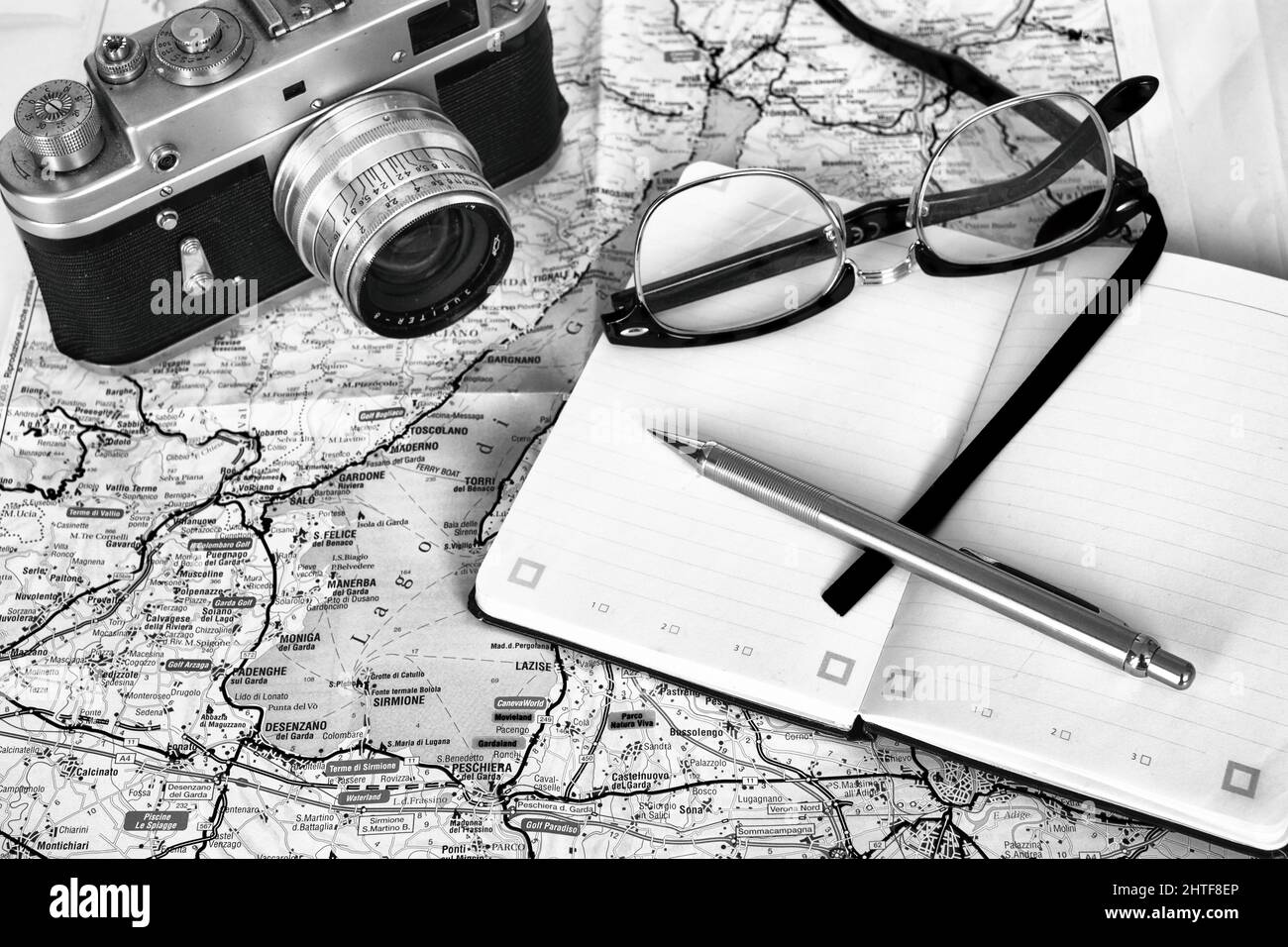 Februar 2022 - Reiseplanung - alte Filmkamera, mit Notizbuch, Brille und einer Landkarte des Gardasees in Italien Stockfoto