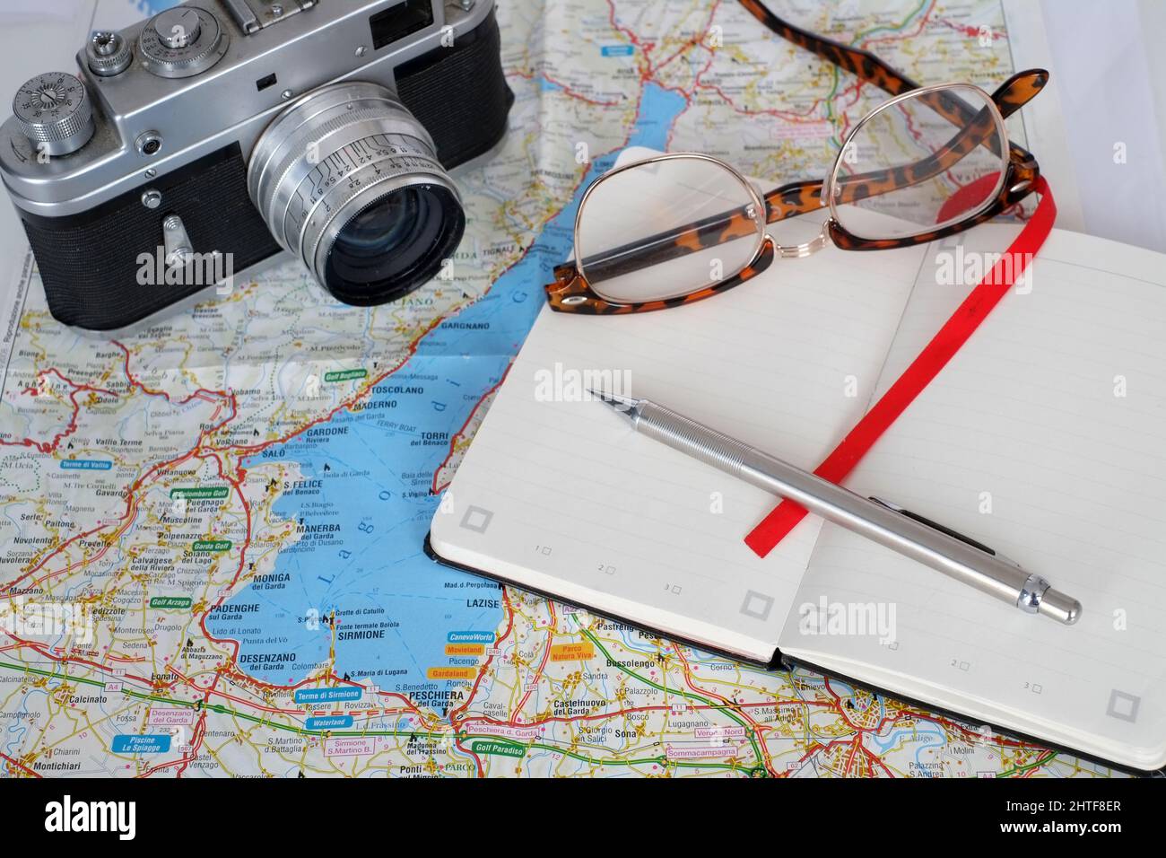 Februar 2022 - Reiseplanung - alte Filmkamera, mit Notizbuch, Brille und einer Landkarte des Gardasees in Italien Stockfoto
