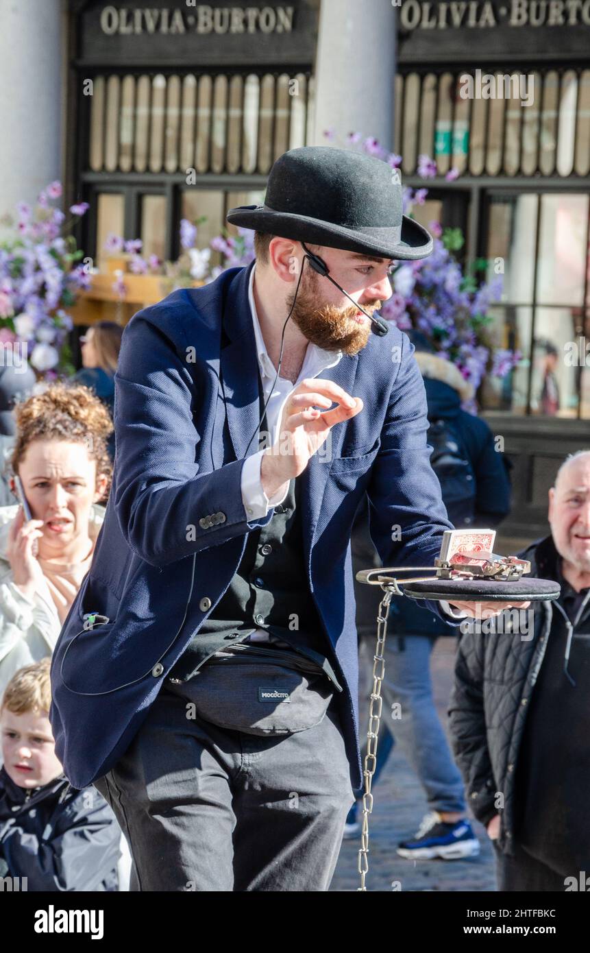 Ein Straßenkünstler mit einem Melone-Hut, der einen Kartentrick macht, um eine Menge im Covent Garden in London, Großbritannien, zu unterhalten Stockfoto