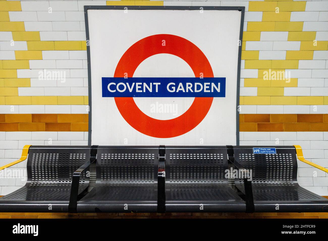 Ein Symbol der Londoner U-Bahn an der Wand des Bahnhofs Covent Garden über einer Sitzreihe. Stockfoto