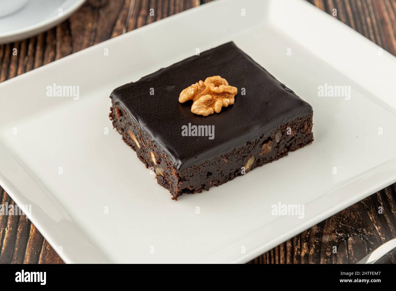 Nussbaum und dunkler Schokoladenbrownie auf einem weißen Porzellanteller auf einem Holztisch Stockfoto