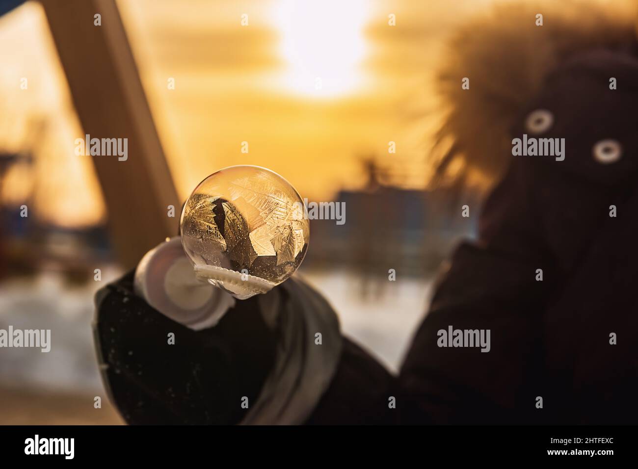 Ein Mädchen hält eine Seifenblase mit schönen Frostmustern in den Strahlen der Sonne Stockfoto