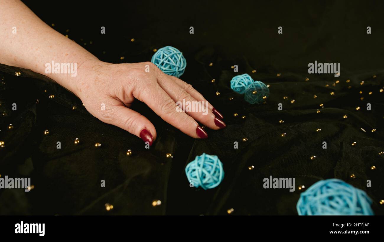 Reife Frauenhand mit rot polierten Nägeln auf schwarzem Hintergrund mit Dekor. Nicht erkennbare Person mit Maniküre beschneiden. Konzept von Pflege und Schönheit Stockfoto