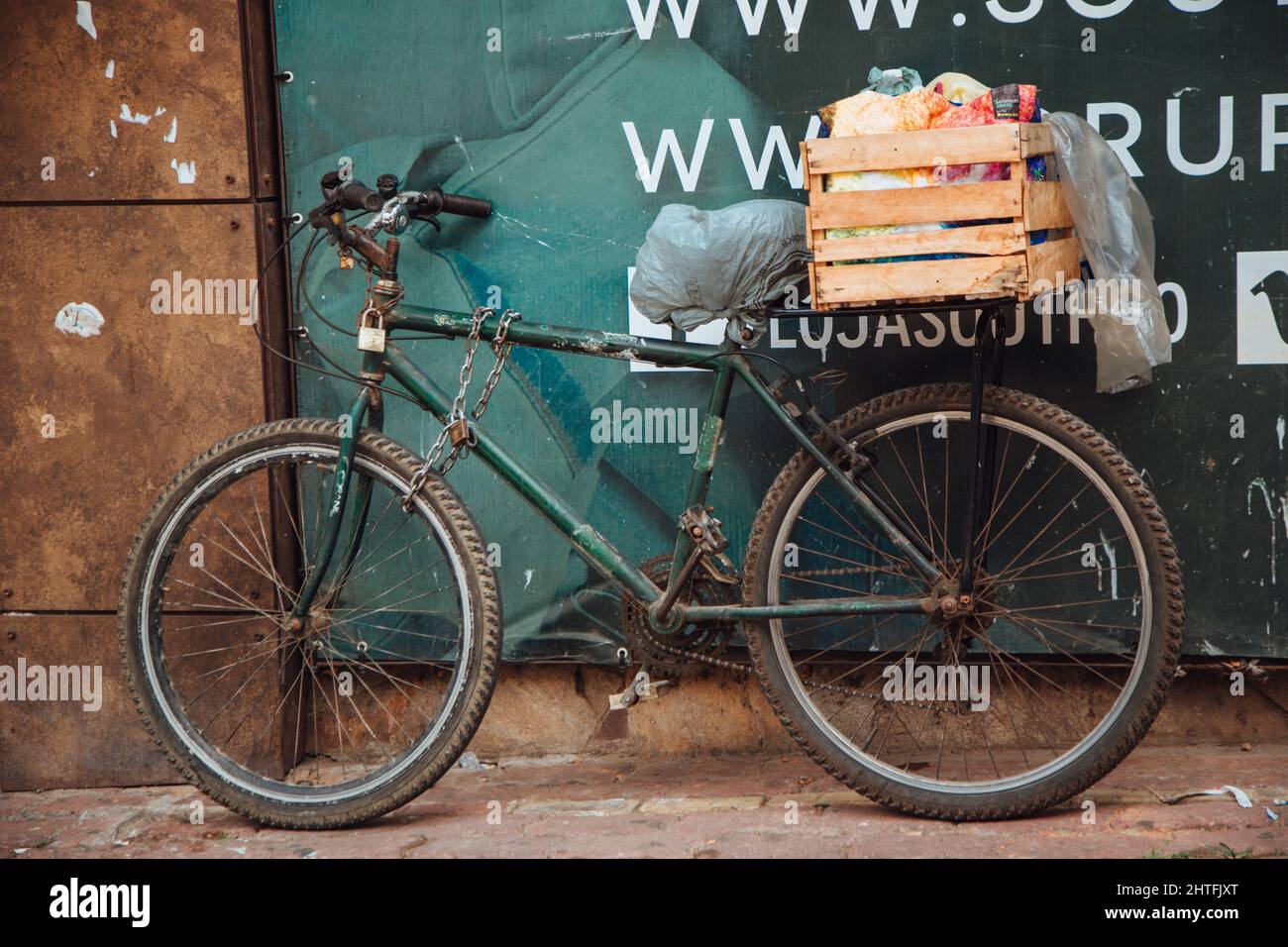 Altes schwarzes Fahrrad mit hölzernen Sachen im Hintergrund, die an einer alten Metalltür im Freien gelehnt sind Stockfoto