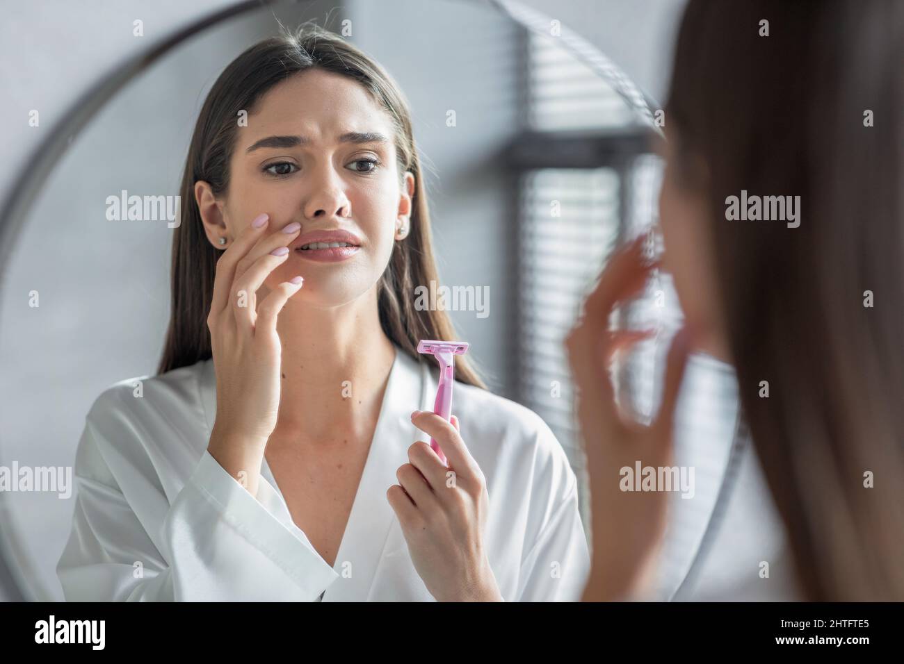 Gesichtshaardepilation. Verwirrt Lady Mit Rasiermesser In Der Hand Blick Auf Spiegel Stockfoto