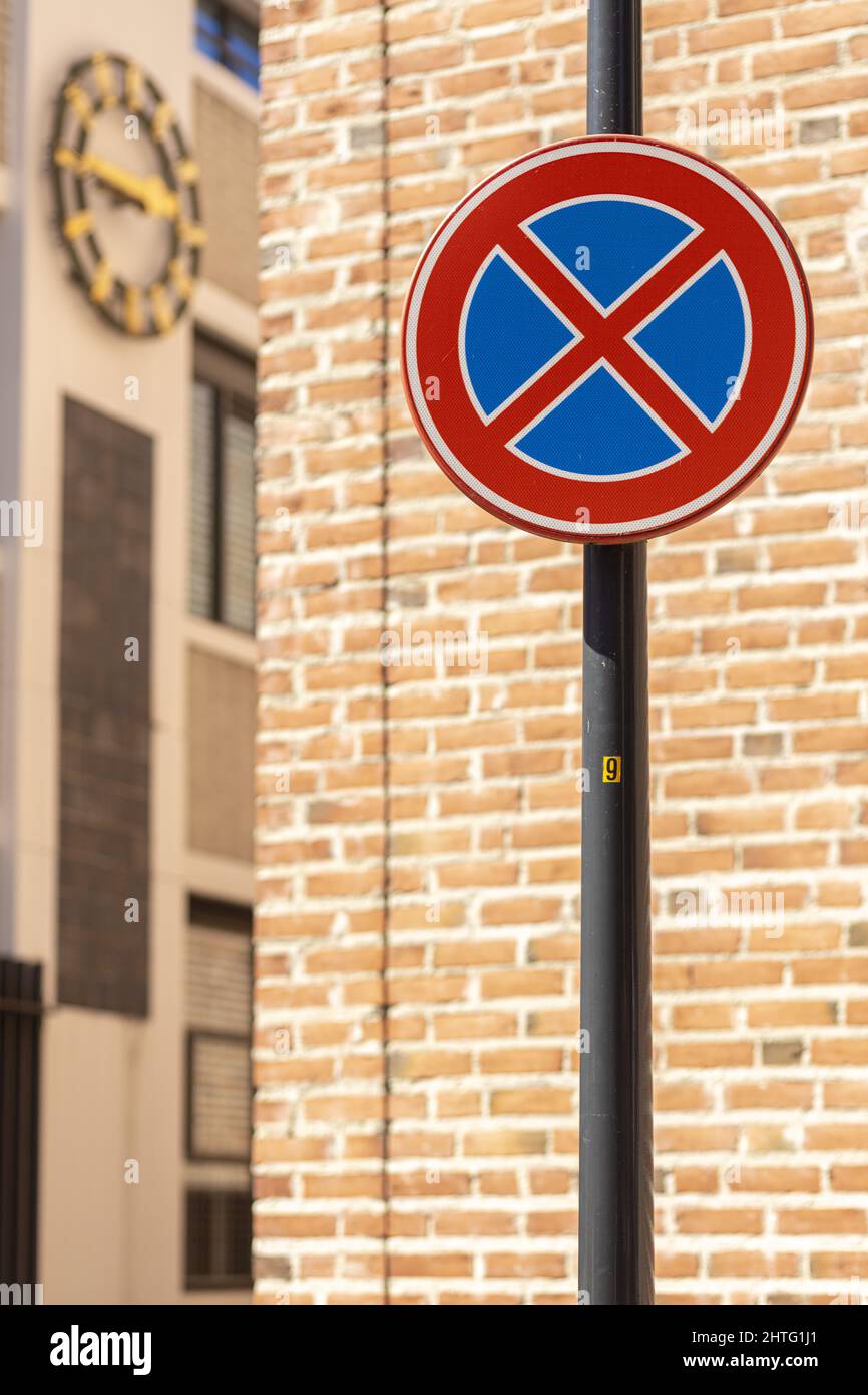 Rundes Verkehrsschild vor Backsteinmauer und Uhr mit durchgestrichenen blauen Formen, was bedeutet, dass es nicht erlaubt ist, zu parken oder gar still zu stehen Stockfoto