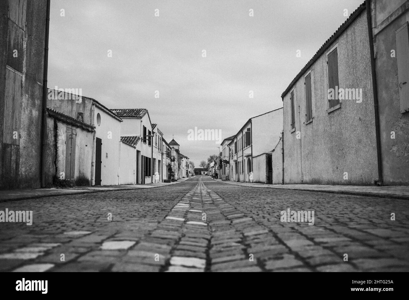 Eine Graustufe von alten Häusern entlang einer leeren Kopfsteinpflasterstraße Stockfoto