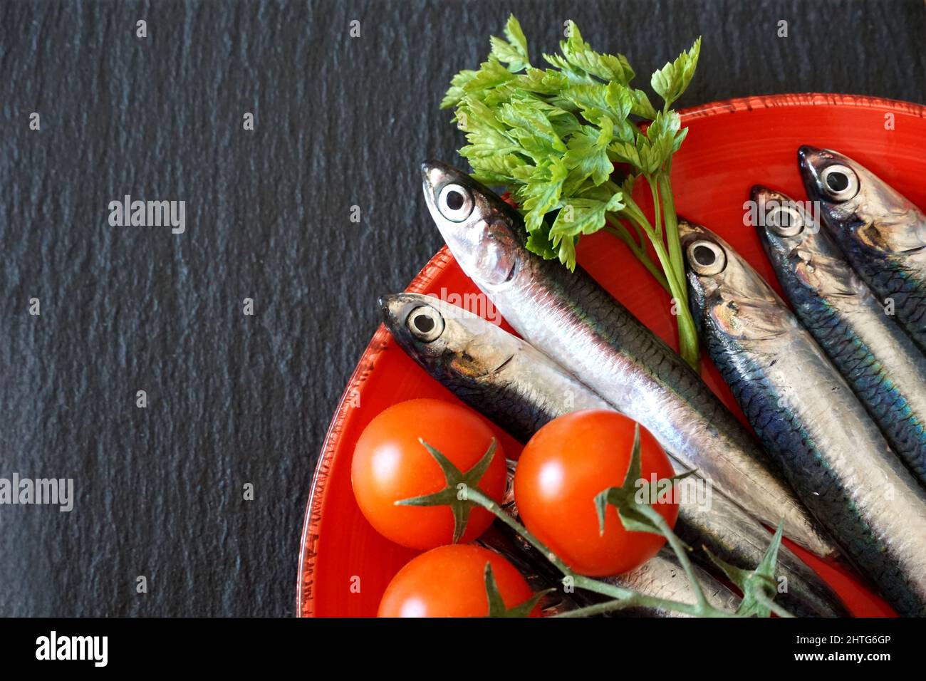 Sardellen auf der res-Platte. Roher und frischer kleiner Meeresfisch, flach auf dem schwarzen Küchentafel liegend, freier Kopierplatz Stockfoto
