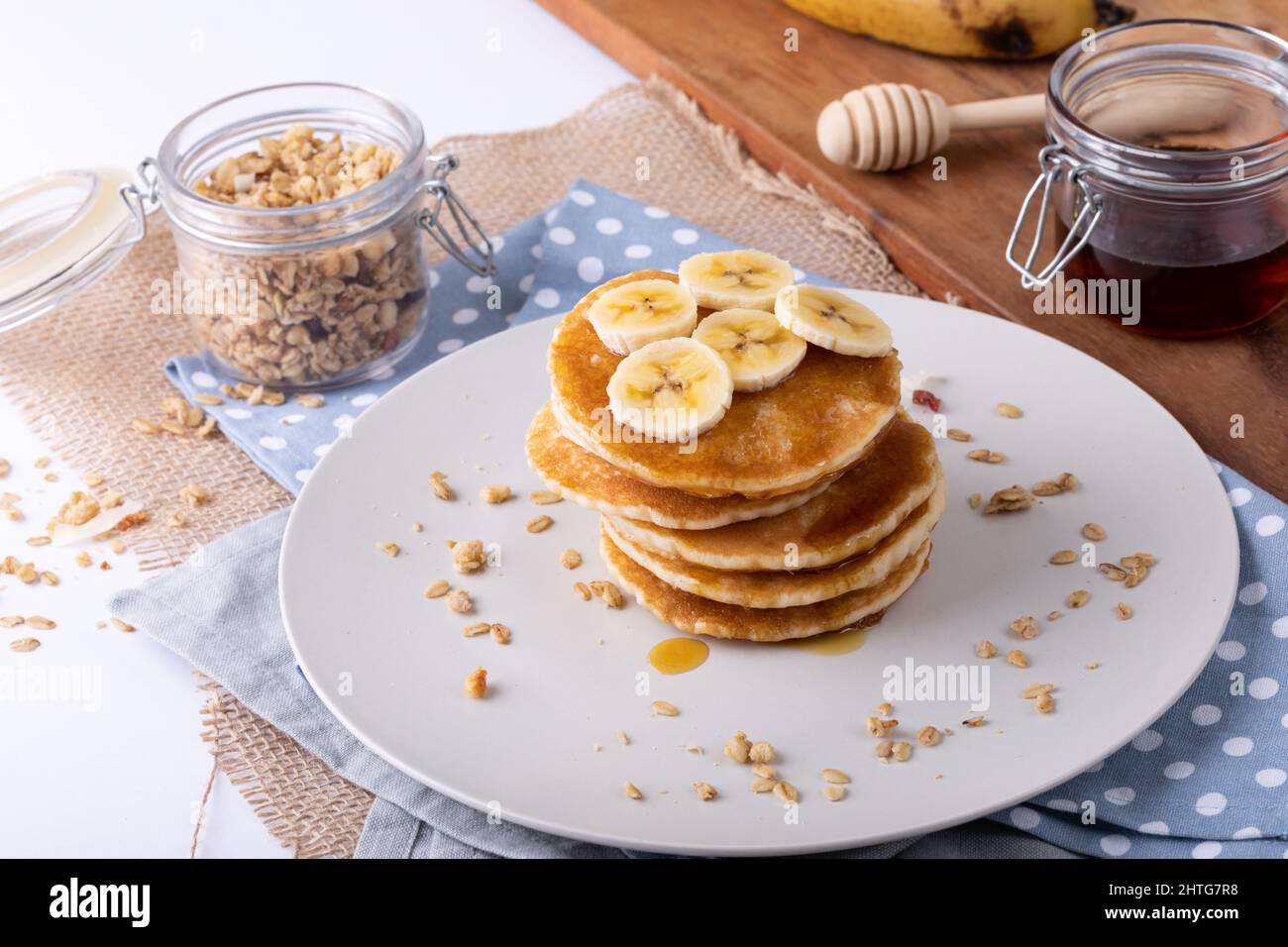 Blick aus der Perspektive auf Bananenscheiben über Pfannkuchen, serviert auf Serviette von Haferflocken und Honigglas Stockfoto