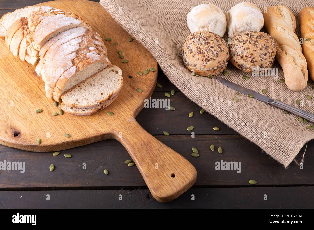 Blick aus der Perspektive auf Brotscheiben auf dem Servierbrett mit Brötchen und Baguettes auf Jute-Stoff Stockfoto