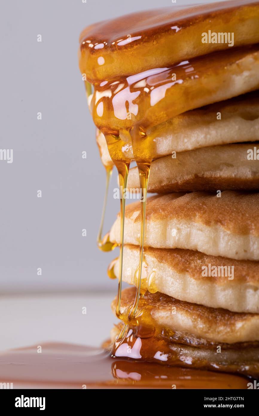 Nahaufnahme von verlockenden, gestapelten Pfannkuchen mit tropfendem Sirup vor grauem Hintergrund Stockfoto