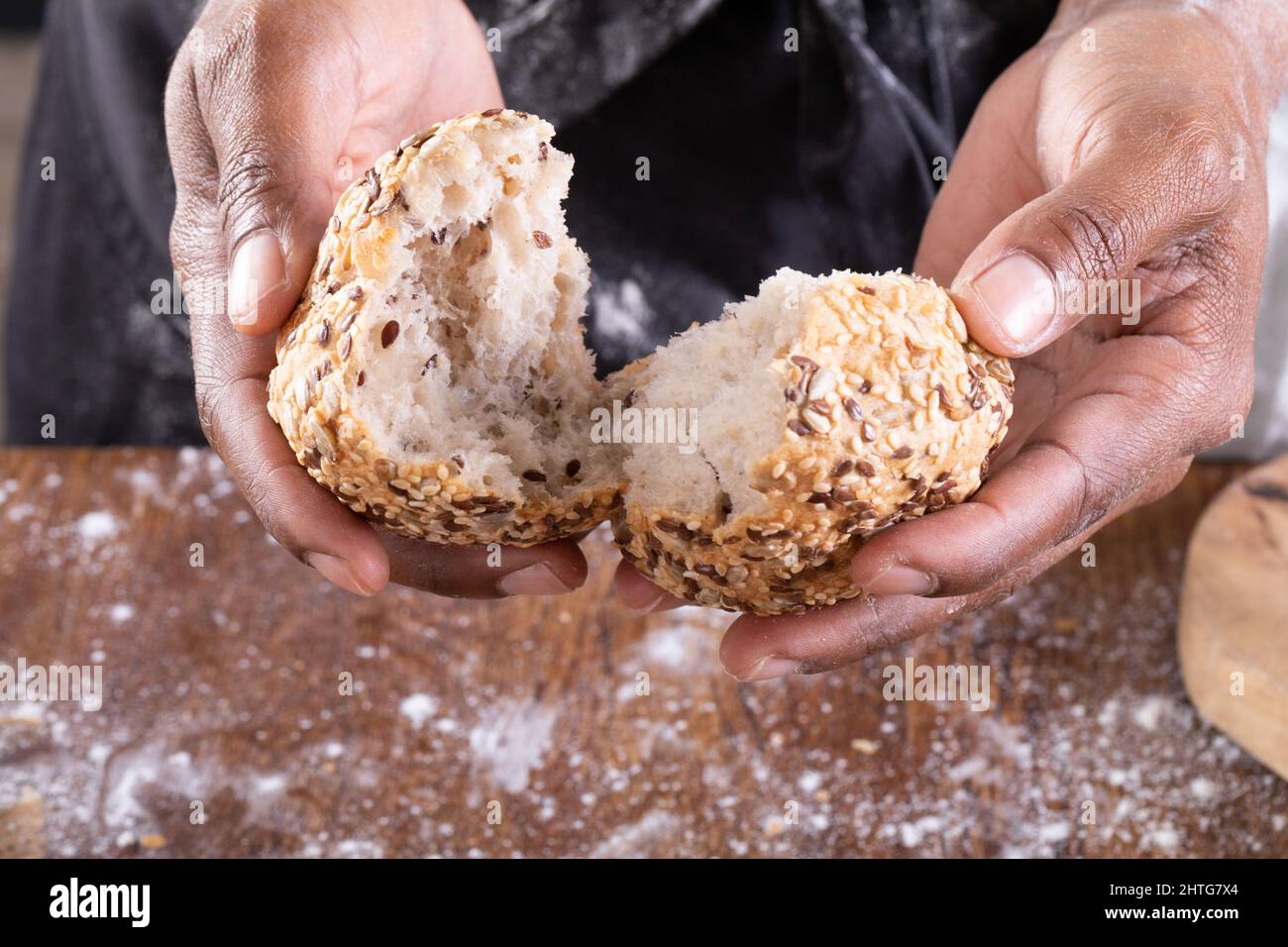 Nahaufnahme eines afroamerikanischen männlichen Bäckers, der Brot auf den Tisch brach Stockfoto