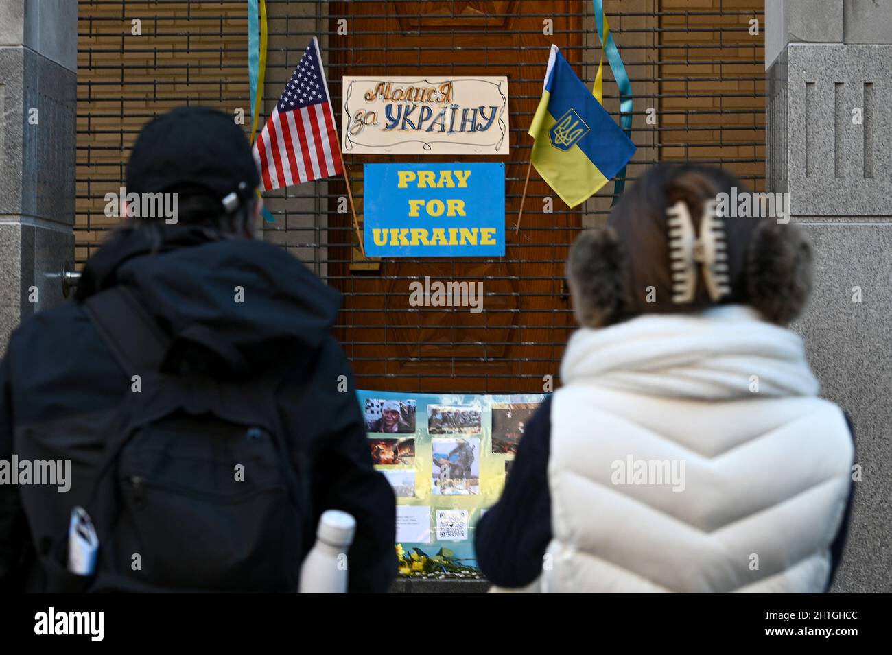 New York, USA. 28.. Februar 2022. Zwei Menschen halten an, um sich ein kleines Denkmal mit Blumen und Fahnen anzusehen, das am Tor der St. George Ukrainischen Katholischen Kirche für Ukrainer errichtet wurde, die unter den Auswirkungen des Krieges leiden, der durch eine Invasion aus Russland, New York, NY, am 28. Februar 2022 verursacht wurde. Der russische Präsident Wladimir Putin begann in den frühen Morgenstunden des 24. Februar mit der Invasion in die benachbarte Ukraine. (Foto von Anthony Behar/Sipa USA) Quelle: SIPA USA/Alamy Live News Stockfoto