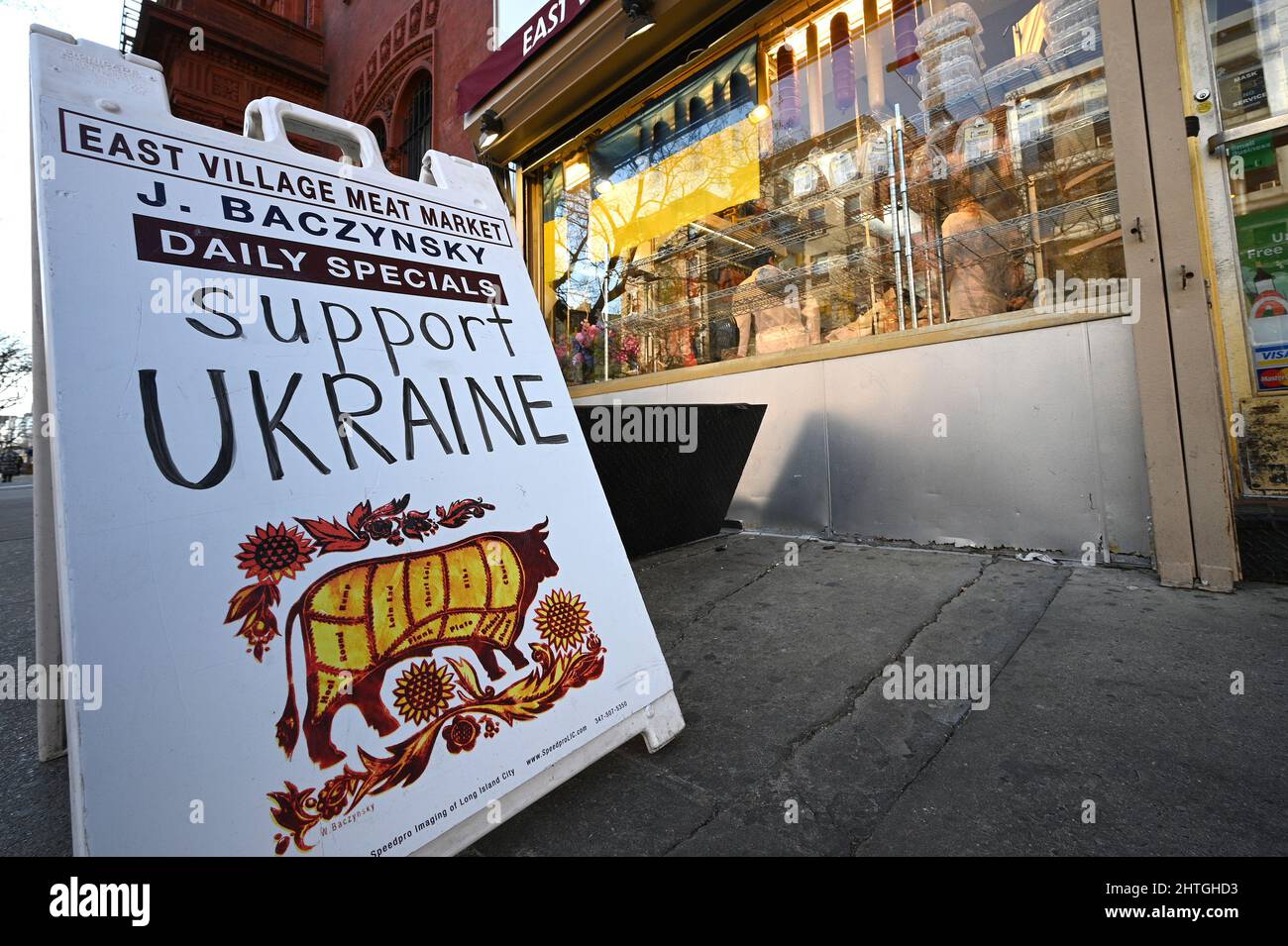 New York, USA. 28.. Februar 2022. Vor dem J. Baczynsky Meat Market sind das Zeichen „Unterstützung der Ukraine“ und eine ukrainische Flagge zu sehen, die ihre Unterstützung für die Ukraine nach dem Einmarsch von Russland, New York, NY, 28. Februar 2022, markieren. Der russische Präsident Wladimir Putin begann in den frühen Morgenstunden des 24. Februar mit der Invasion in die benachbarte Ukraine. (Foto von Anthony Behar/Sipa USA) Quelle: SIPA USA/Alamy Live News Stockfoto
