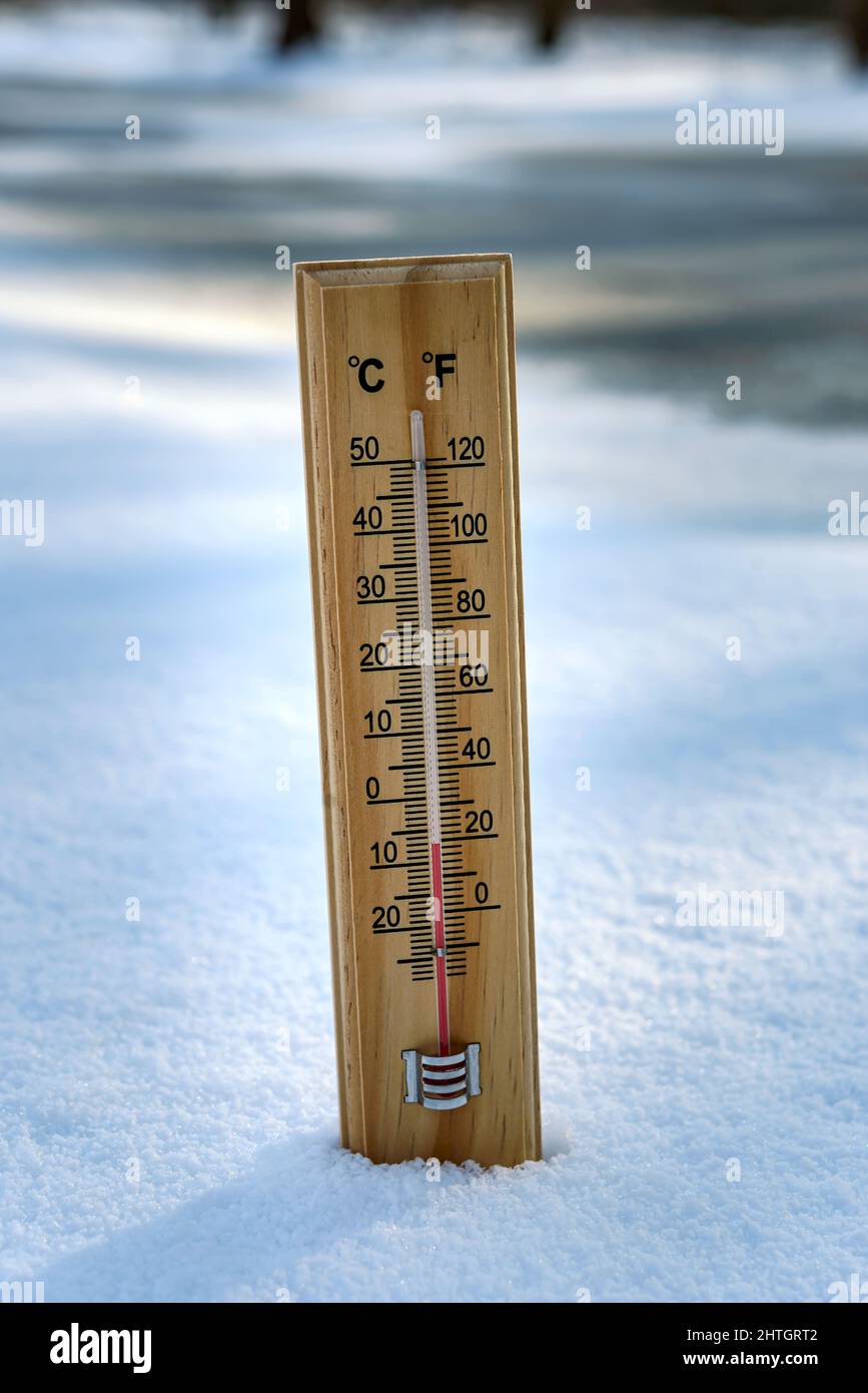 Das Quecksilberthermometer aus Holz, das auf Schnee hängt, weist niedrige Temperaturen auf. Stockfoto