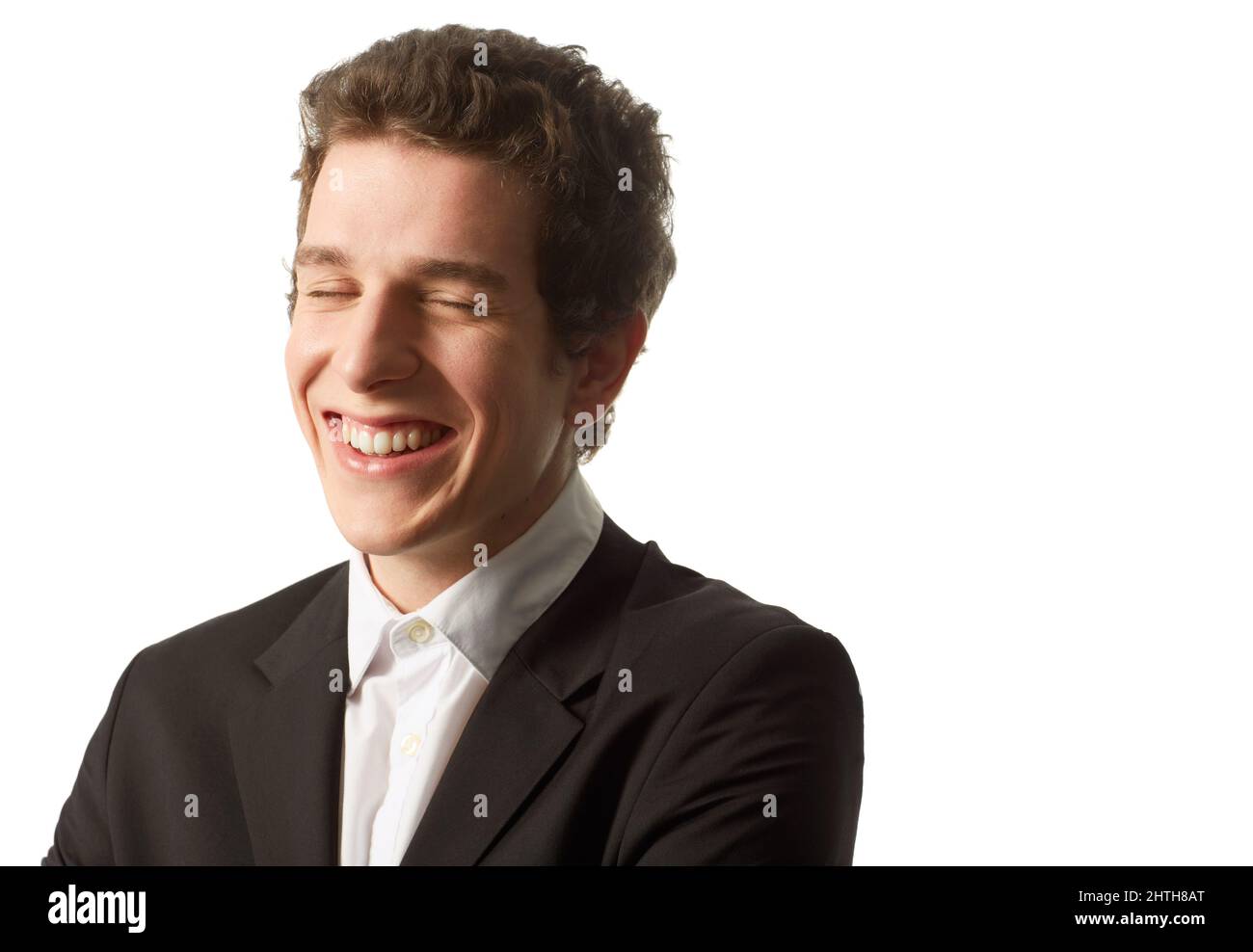 Aufrichtiges Lächeln. Ein junger Mann, der ein knöpftes Hemd und eine Jacke trägt, lacht, während er vor einem weißen Hintergrund steht. Stockfoto