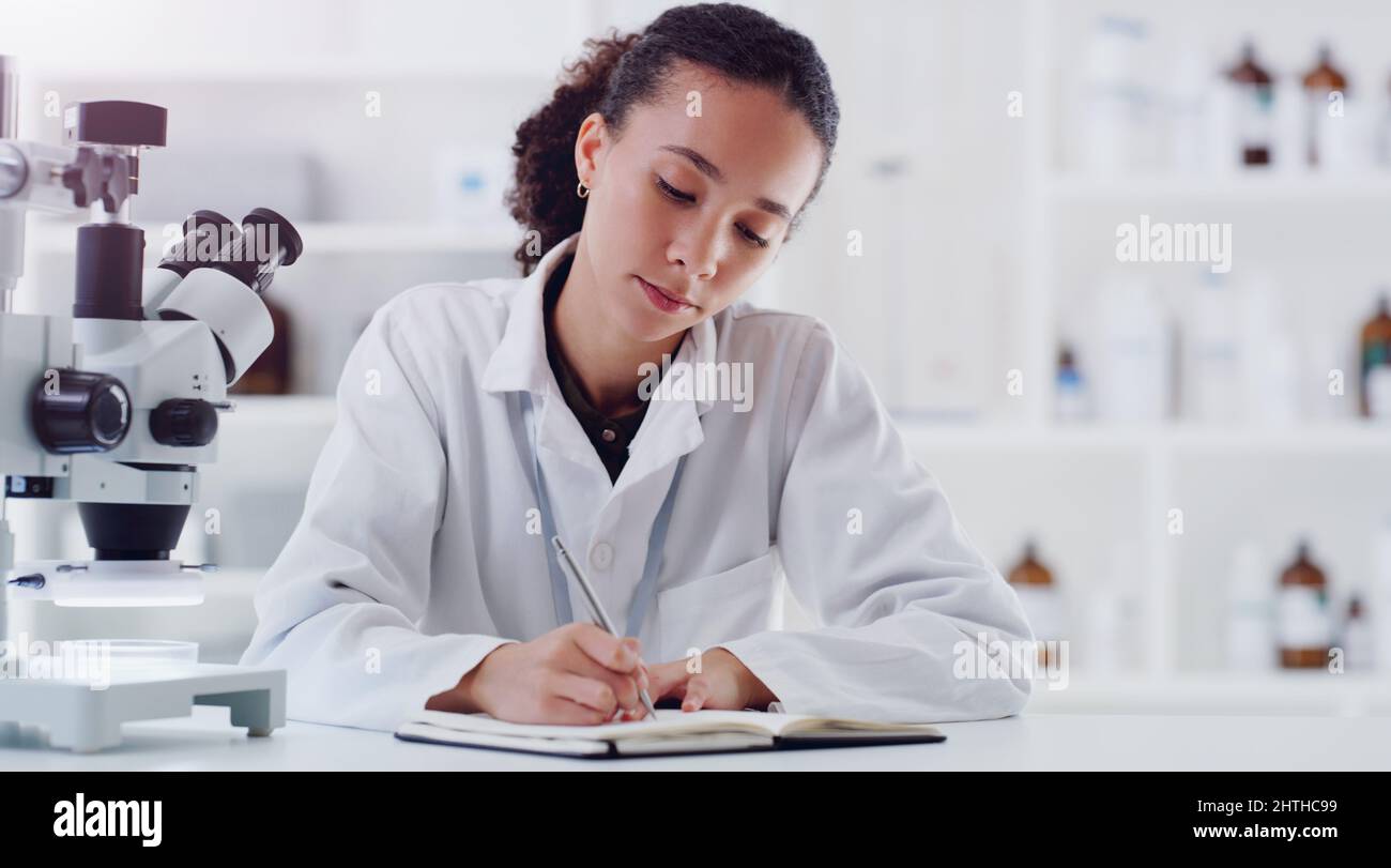 Untersuchen einer Angelegenheit nach der anderen. Aufnahme eines jungen Wissenschaftlers, der während der Arbeit in einem Labor Notizen schreibt. Stockfoto