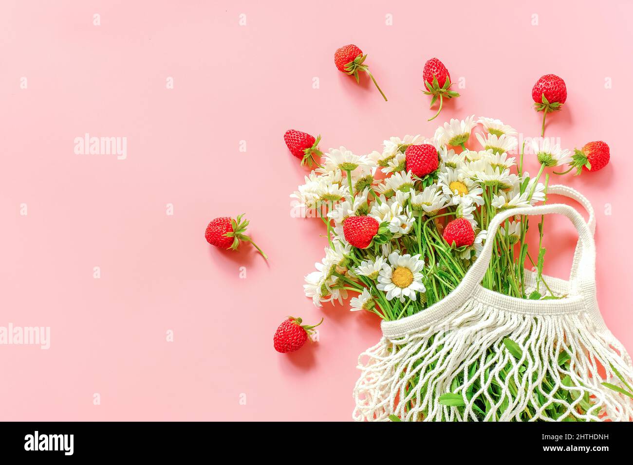 Bouquet von Feldblumenstrauß im wiederverwendbaren Einkaufstasche aus Öko-Mesh und roten Erdbeeren auf rosa Hintergrund. Konzept kein Kunststoff und kein Abfall. Platz oben kopieren Stockfoto