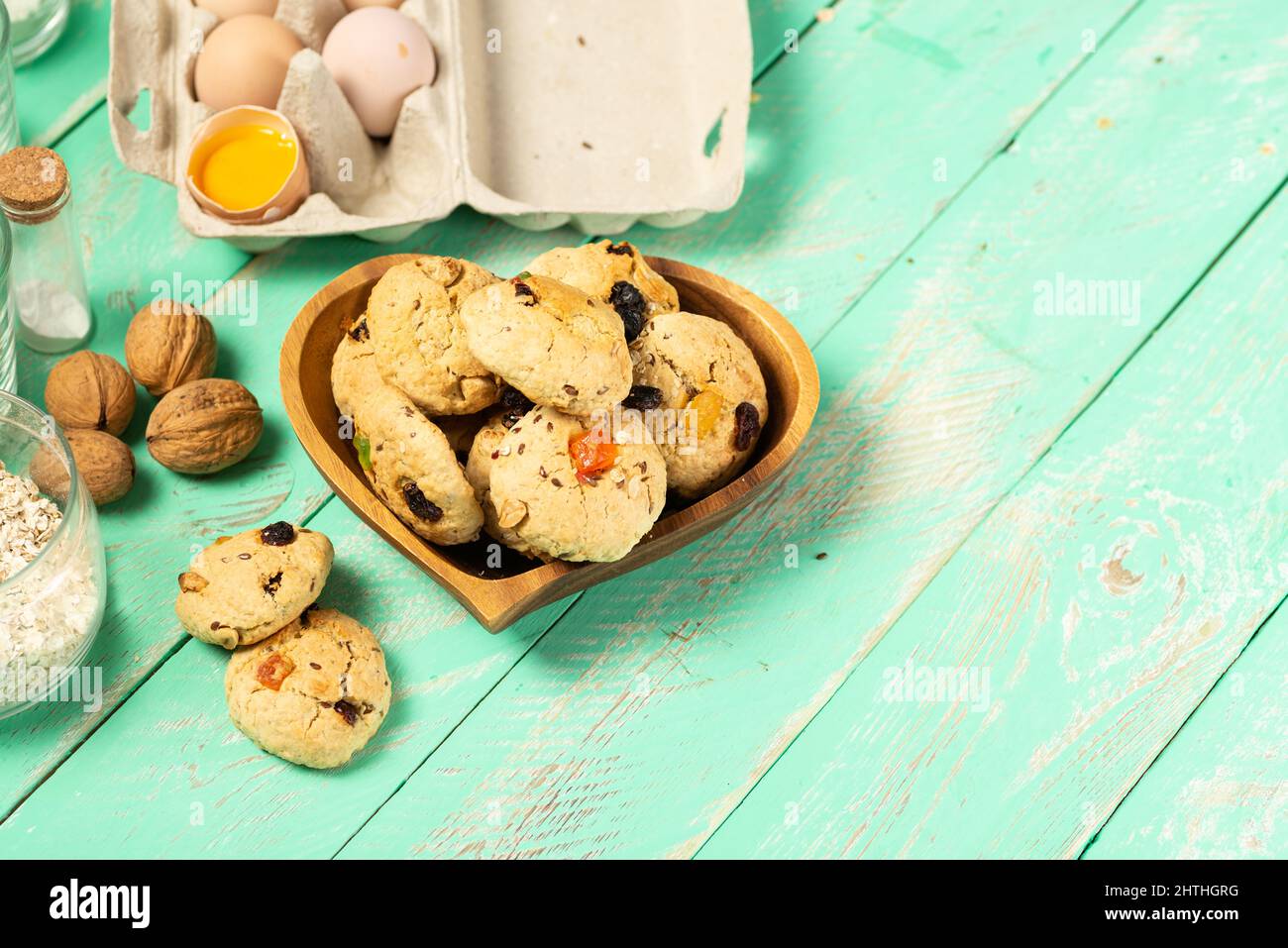 Kochen Haferflockenkekse mit kandierten Früchten und Walnüssen. Eier, Haferflocken, Mehl, Zucker, Gewürze und Küchenutensilien auf einem alten Holz. Backrezept oder Stockfoto