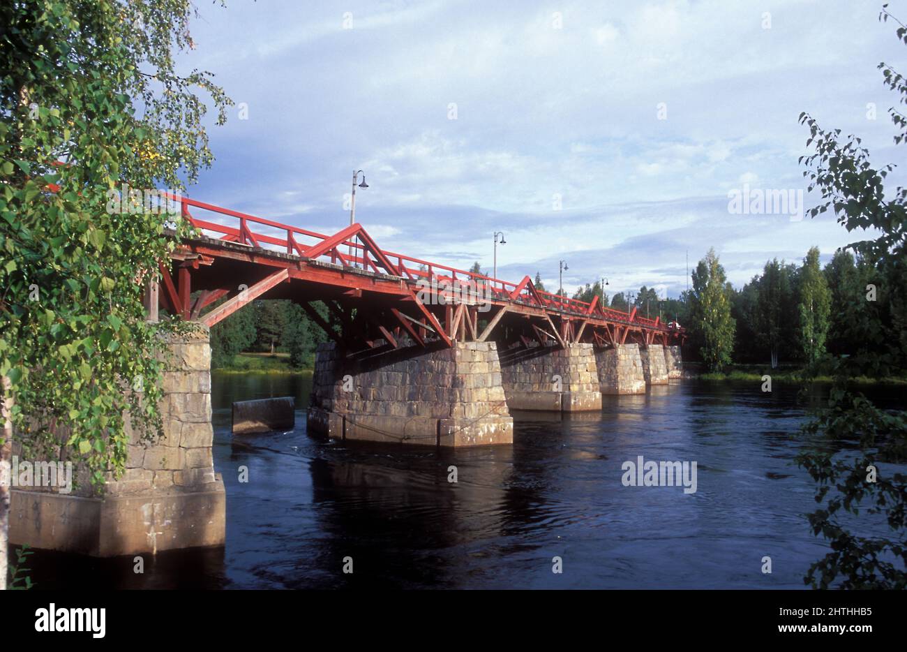 Rote Holzbrücke überquert einen Fluss, analog. Basierend auf großen Steinen und Fundamenten im Fluss. Stockfoto