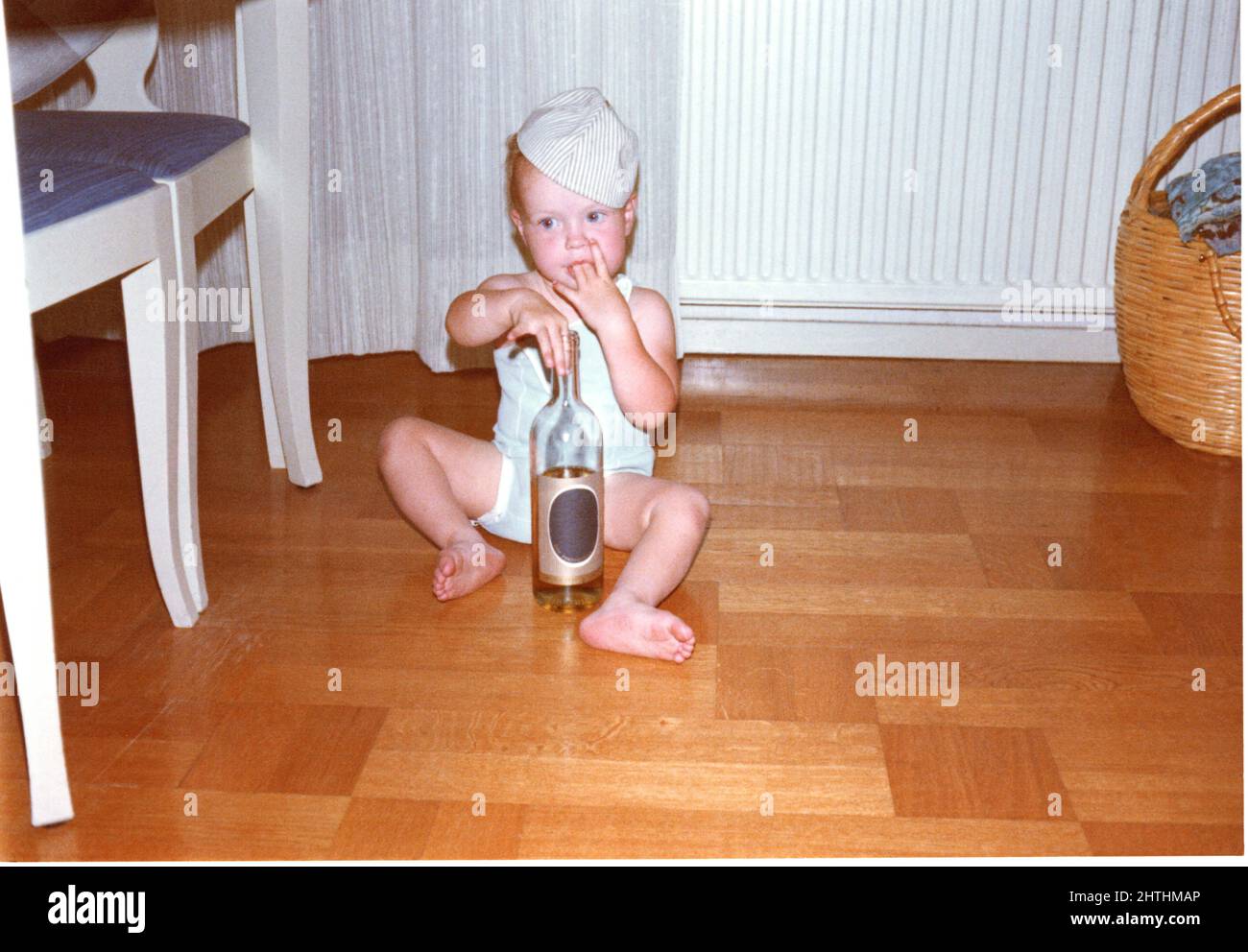 Foto des kleinen Kindes aus den 1960er Jahren, das mit einer Glasflasche auf einem Holzboden spielt, Schweden. Stockfoto