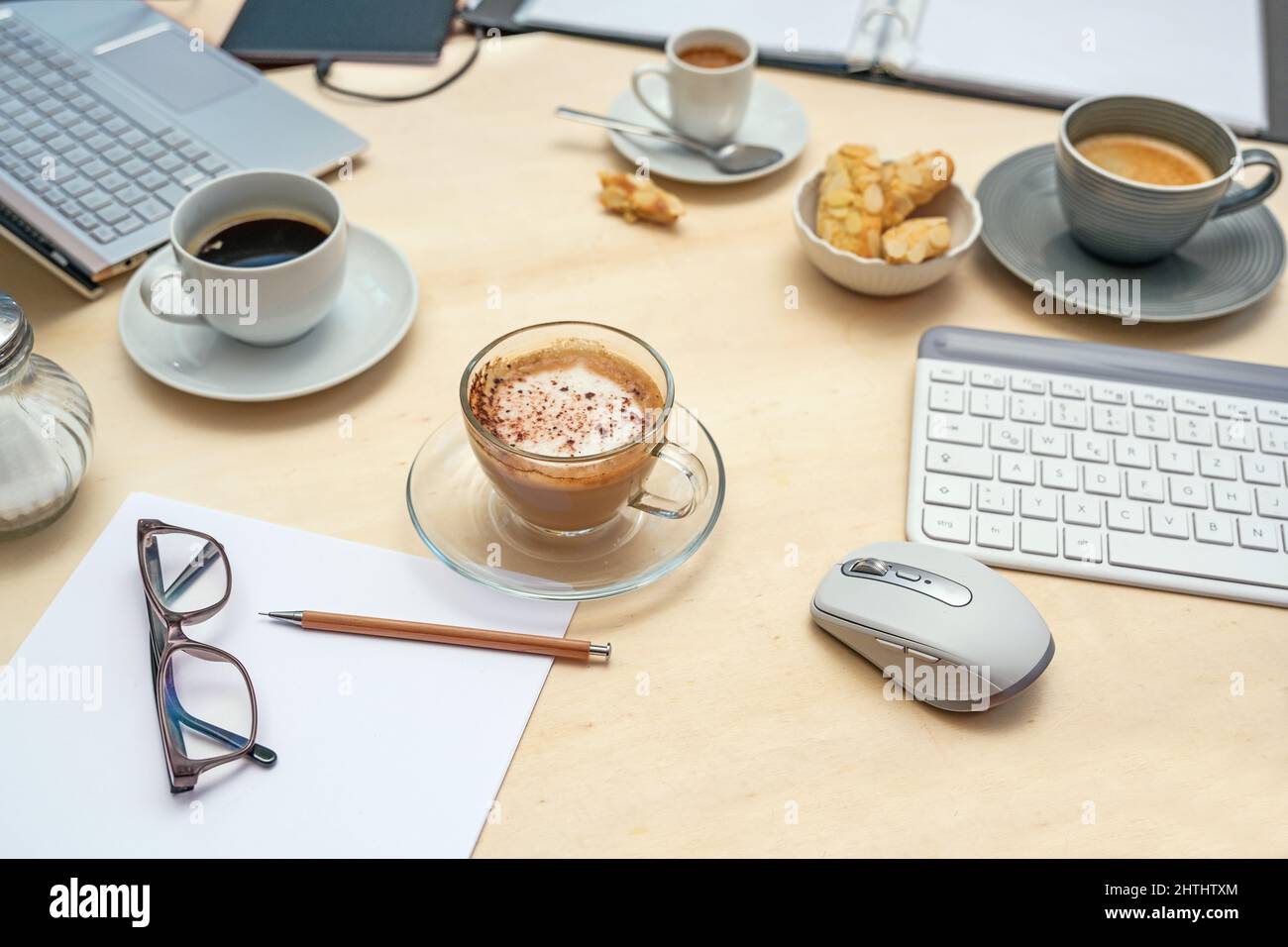 Tisch bei einem Meeting mit Laptop, Tastatur, Ordner und Papieren und verschiedenen Kaffeetassen, hellem Holz, niemand, ausgewählter Fokus, enge Schärfentiefe Stockfoto