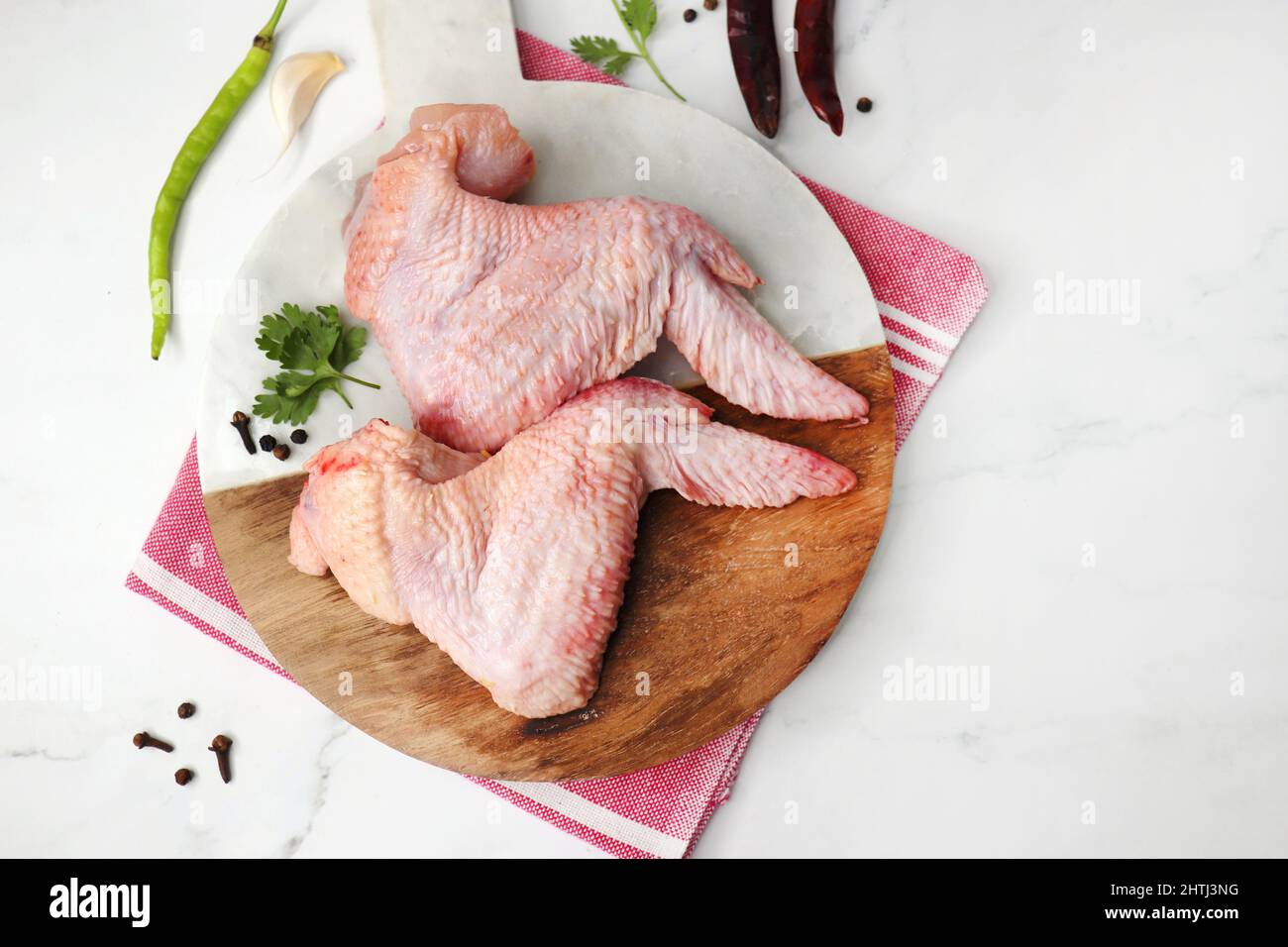 Rohe Hähnchenflügel auf schwarzem Teller zusammen mit Gewürzen wie schwarzem Pfeffer, grünem Chili, rotem Chili und Koriander. Perfekt für die Vorbereitung des Buffalo Wings Stockfoto