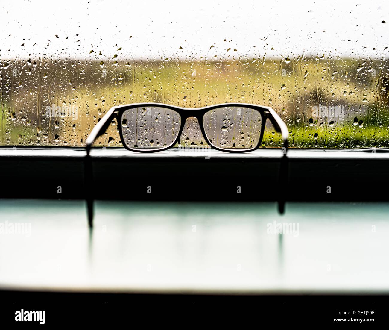 Eine Brille, die auf einer Fensterbank ruht und die widrigen Wetterbedingungen beobachtet. Stockfoto