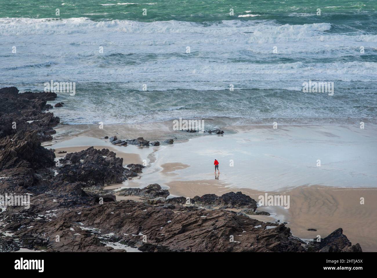 Die kleine Figur einer Person, die an einem windigen Fistral Beach in Newquay in Cornwall entlang der Küste läuft. Stockfoto