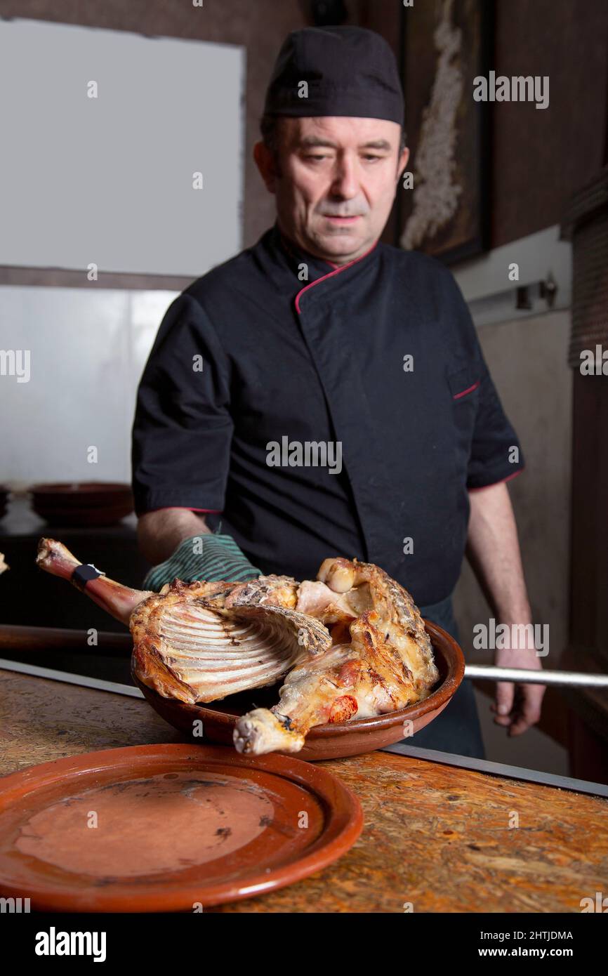 Männlicher Koch, der mit rohem Geflügel am Tisch steht, während er während der Arbeit im Restaurant ein köstliches Gericht in der Nähe des Brennofens zubereitet Stockfoto
