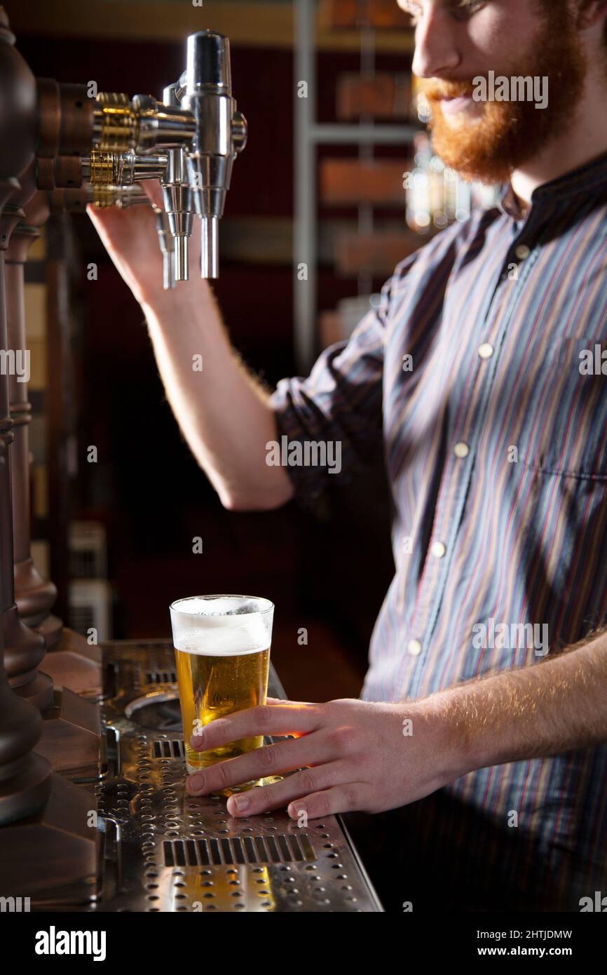 Seitenansicht des abgeschnittenen männlichen Barkeepers mit roten Haaren, die Bier vom Fass in das Glas gießen, während sie während der Arbeit an der Bar an der Theke stehen Stockfoto