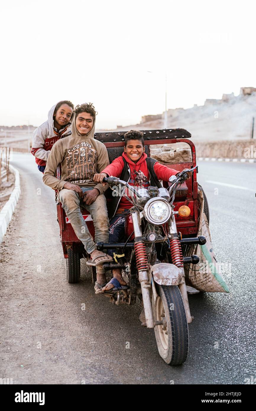 Luxor, Ägypten - 25. Dezember 2021: Entzückende Kinder fahren mit dem Auto auf der Asphaltstraße und sammeln Müll zum Leben Stockfoto