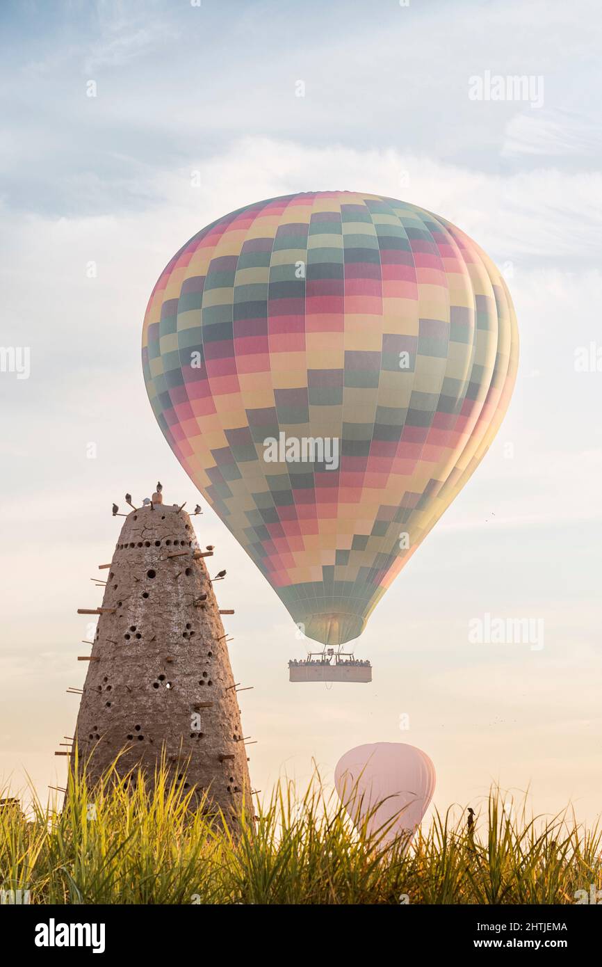 Hoher konischer Nesttaubenturm mit vielen Löchern auf grasbewachsenem Feld mit Luftballons in Ägypten am Sommertag Stockfoto