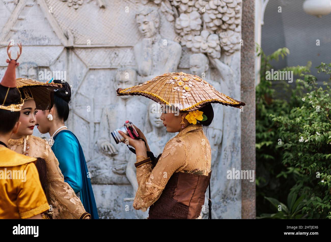 Bangkok, Thailand - 04.20.2017: Ethnische Frau trägt authentische Kostüme und Accessoires und fotografiert im Garten während eines Spaziergangs mit einer Freundin mit der Kamera Stockfoto