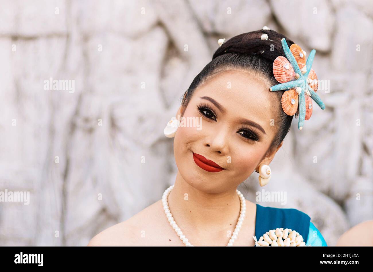 Bangkok, Thailand - 04.20.2017: Lächelndes asiatisches Weibchen mit roten Lippen und originellen Accessoires aus Muscheln und Seesternen auf dem Kopf, die auf Kamera-Agai schauen Stockfoto