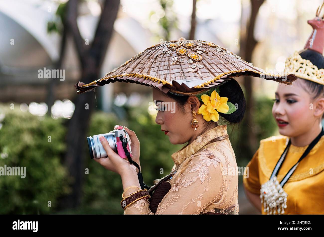Bangkok, Thailand - 04.20.2017: Ethnische Frau trägt authentische Kostüme und Accessoires und fotografiert im Garten während eines Spaziergangs mit einer Freundin mit der Kamera Stockfoto
