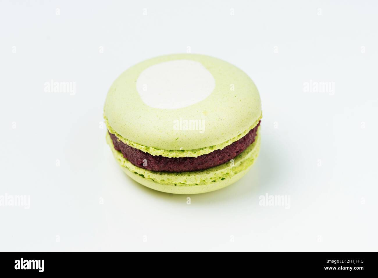 Von oben ein süßer runder grüner Makronen mit weißem Fleck und leckerer Schokoladenfüllung auf weißem Hintergrund im hellen Raum Stockfoto