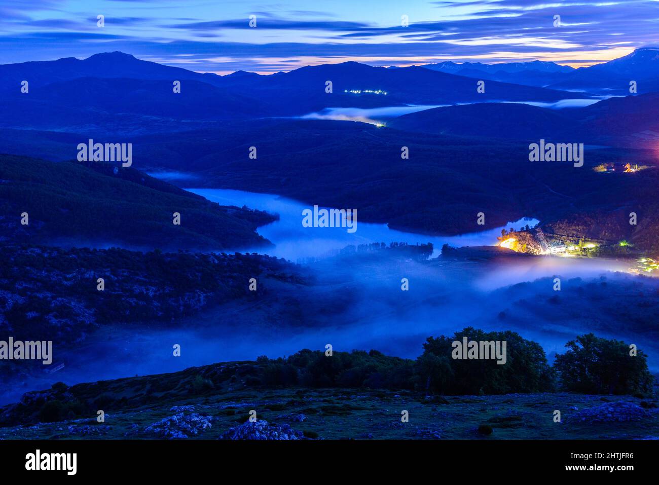 Atemberaubende Landschaft von ruhigen Fluss fließt durch bergiges Tal in der Stadt unter bewölktem Dämmerungshimmel in den Palentian Bergen in Spanien Stockfoto