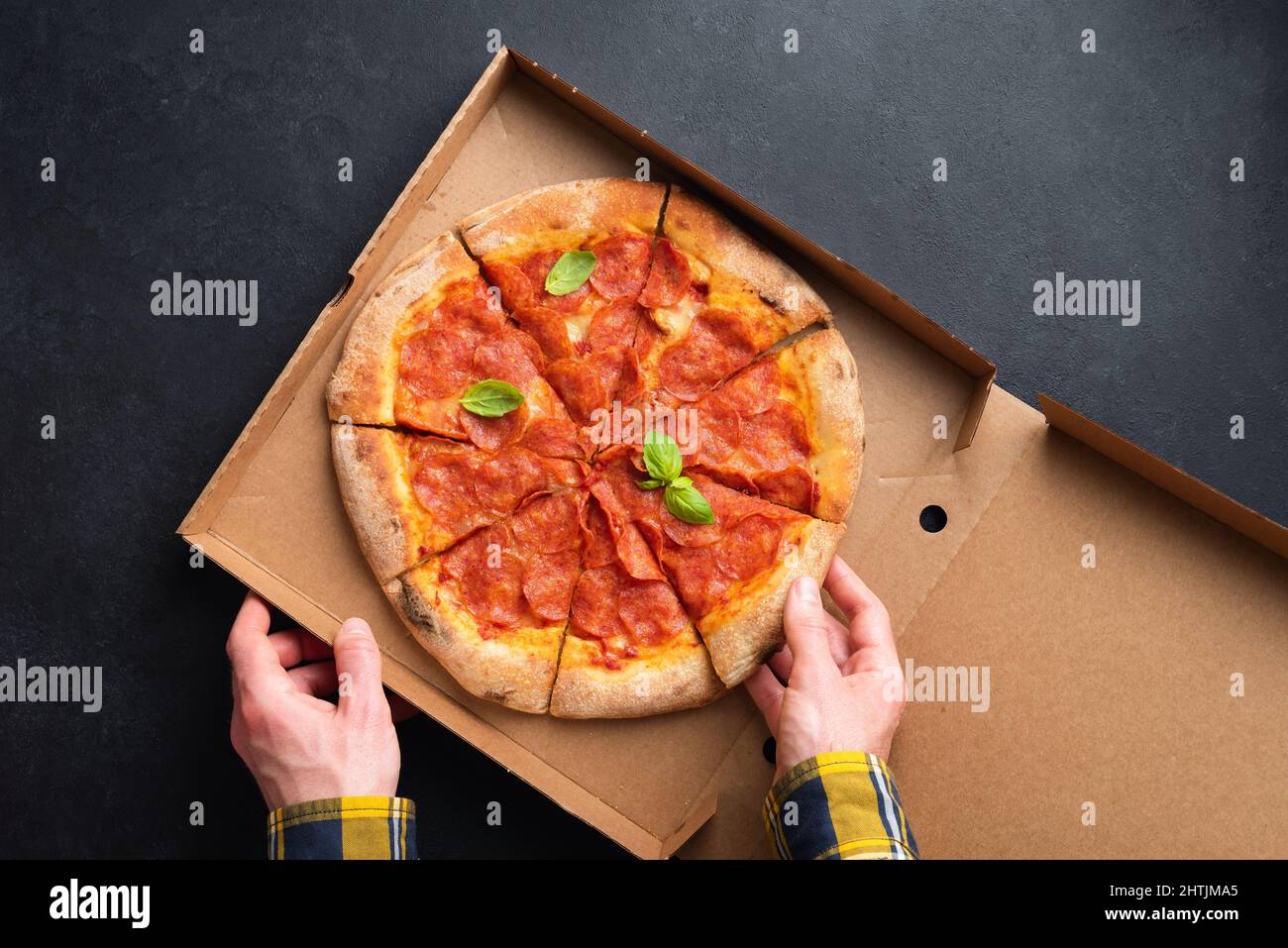 Köstliche Pepperoni Pizza In Karton Karton. Männliche Hände Pflücken Slice Von Hot Pepperoni Pizza, Black Schieferhintergrund. Draufsicht. Koncep Stockfoto