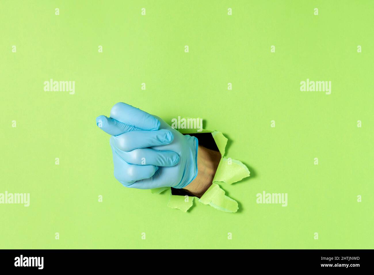 Feige als Handbewegung, die Demütigung oder Verleugnung bezeichnet. Männliche Hand in blauem Latex-Handschuh ragt aus einem zerrissenen Loch in grünem Papier heraus. Speicherplatz kopieren. Stockfoto