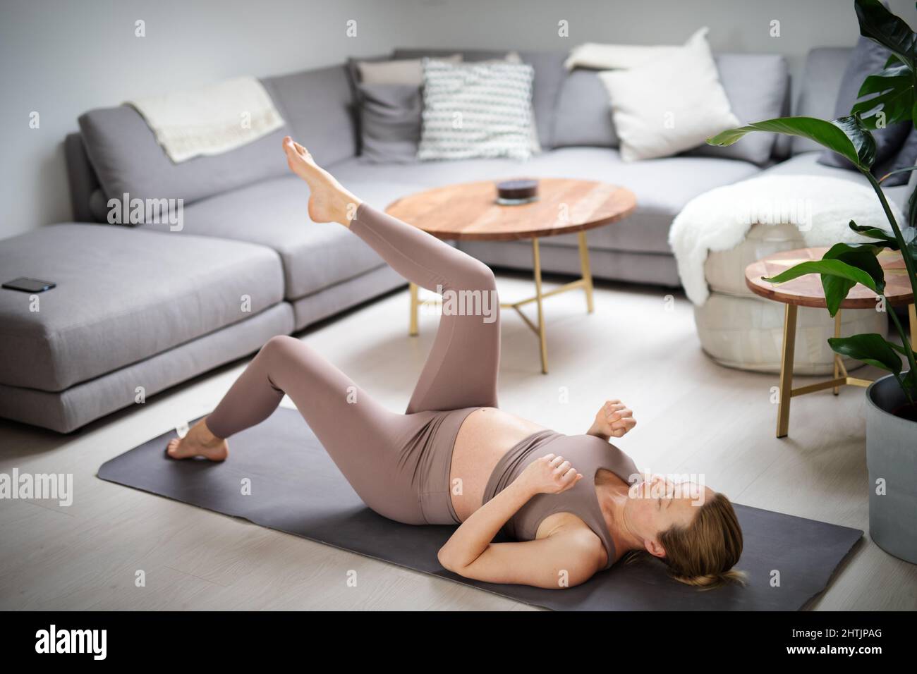 Junge schöne Schwangerin, die zu Hause in ihrem Wohnzimmer Pilates trainiert. Gesunder Lebensstil und aktives Konzept für Schwangerschaft und Mutterschaft. Stockfoto
