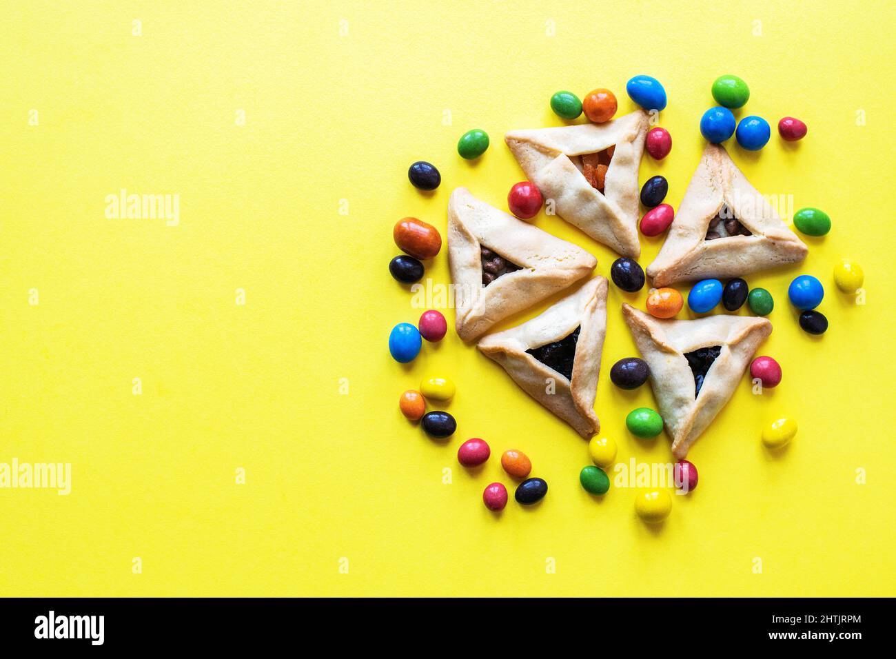 Hamantashen - traditionelle Kekse und bunte Süßigkeiten für jüdische Feiertage Purim. Festliches Backen mit verschiedenen Füllungen auf gelbem Hintergrund. Kopie sp Stockfoto