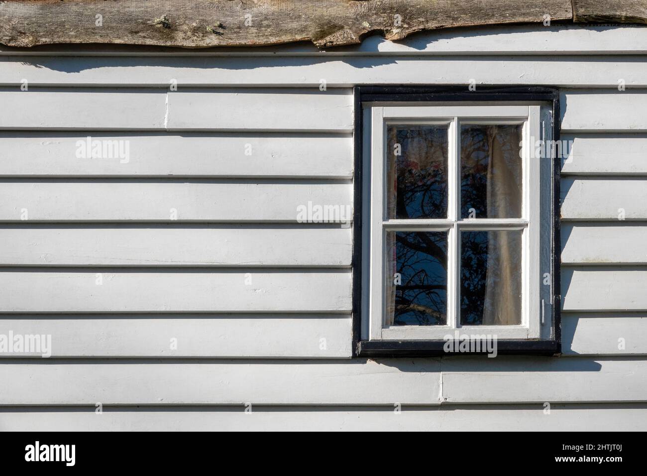Ein kleines, weiß gestrichenes, viergegliedert in eine horizontale, weiß gestrichene Holzverkleidung eingefärbtes Holzfenster, flach darauf, ohne Perspektive Stockfoto