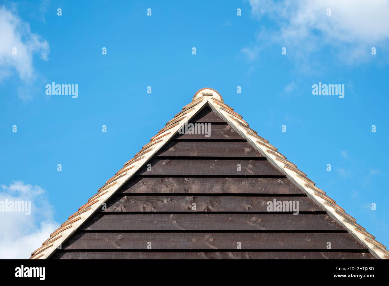 Horizontale Holzverkleidung am Giebel-Ende des Gebäudes mit Ziegeldach, das eine Pyramide gegen einen blauen Himmel bildet Stockfoto
