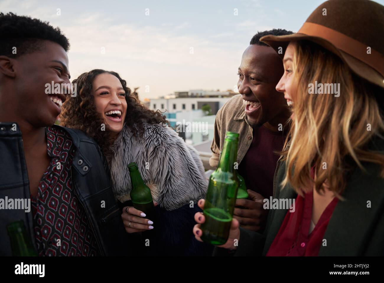 Lachende Gruppe multikultureller junger Erwachsener auf einer Dachterrasse in der Stadt. Lächelt mit Freunden. Stockfoto