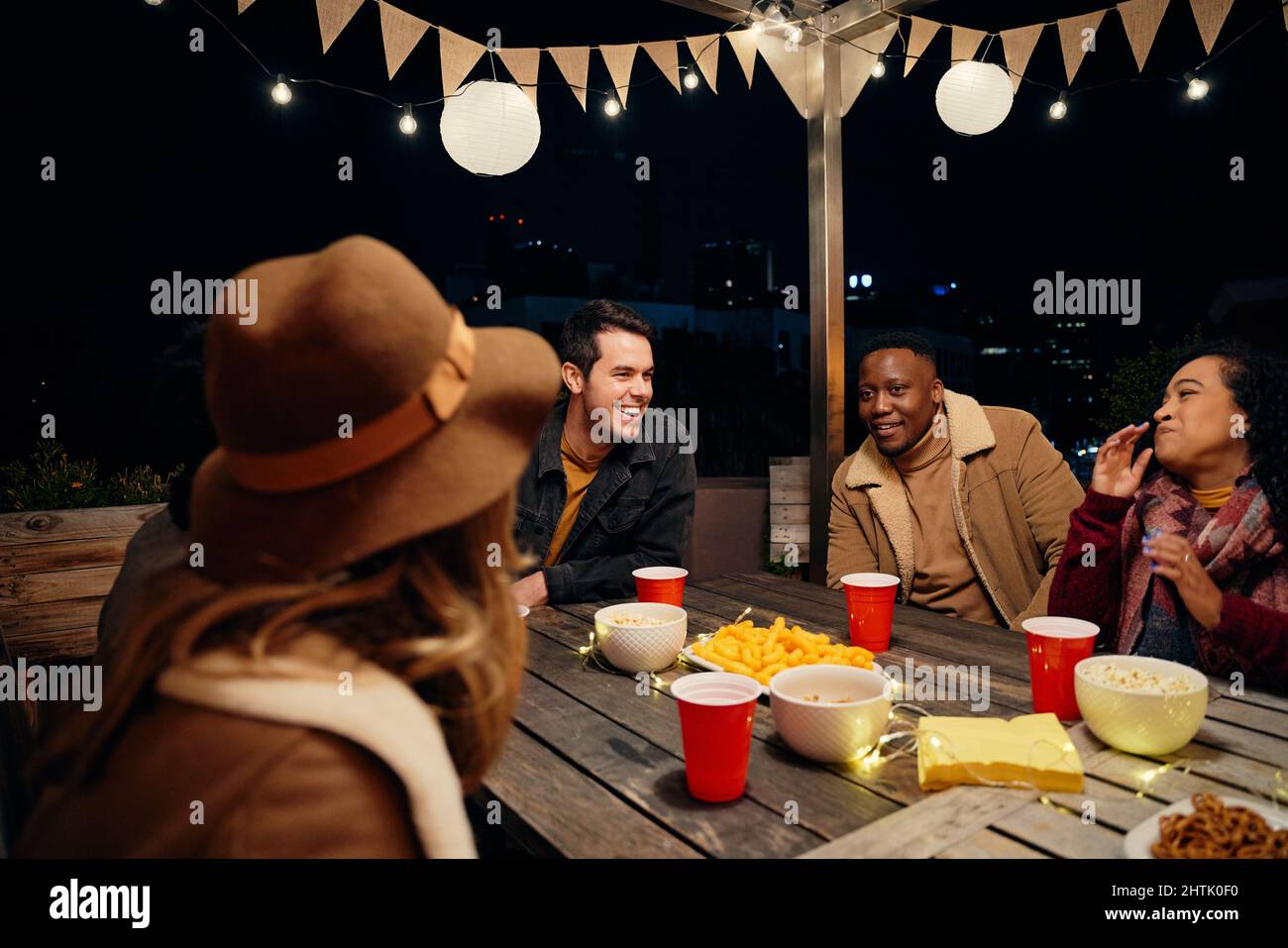 Multikulturelle Gruppe junger erwachsener Freunde, die bei einer trendigen Dachparty am Tisch lachen. Essen und Trinken, eine gute Zeit haben Stockfoto