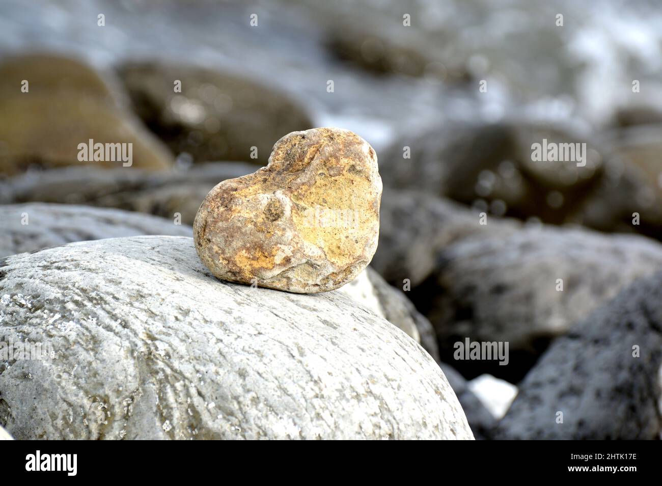 Herzförmiger Stein vor dem Hintergrund des Strandes. Sommersonntag. Liebe, Hochzeit und Valentinstag Konzept. Schöne und interessante Steine finden Stockfoto