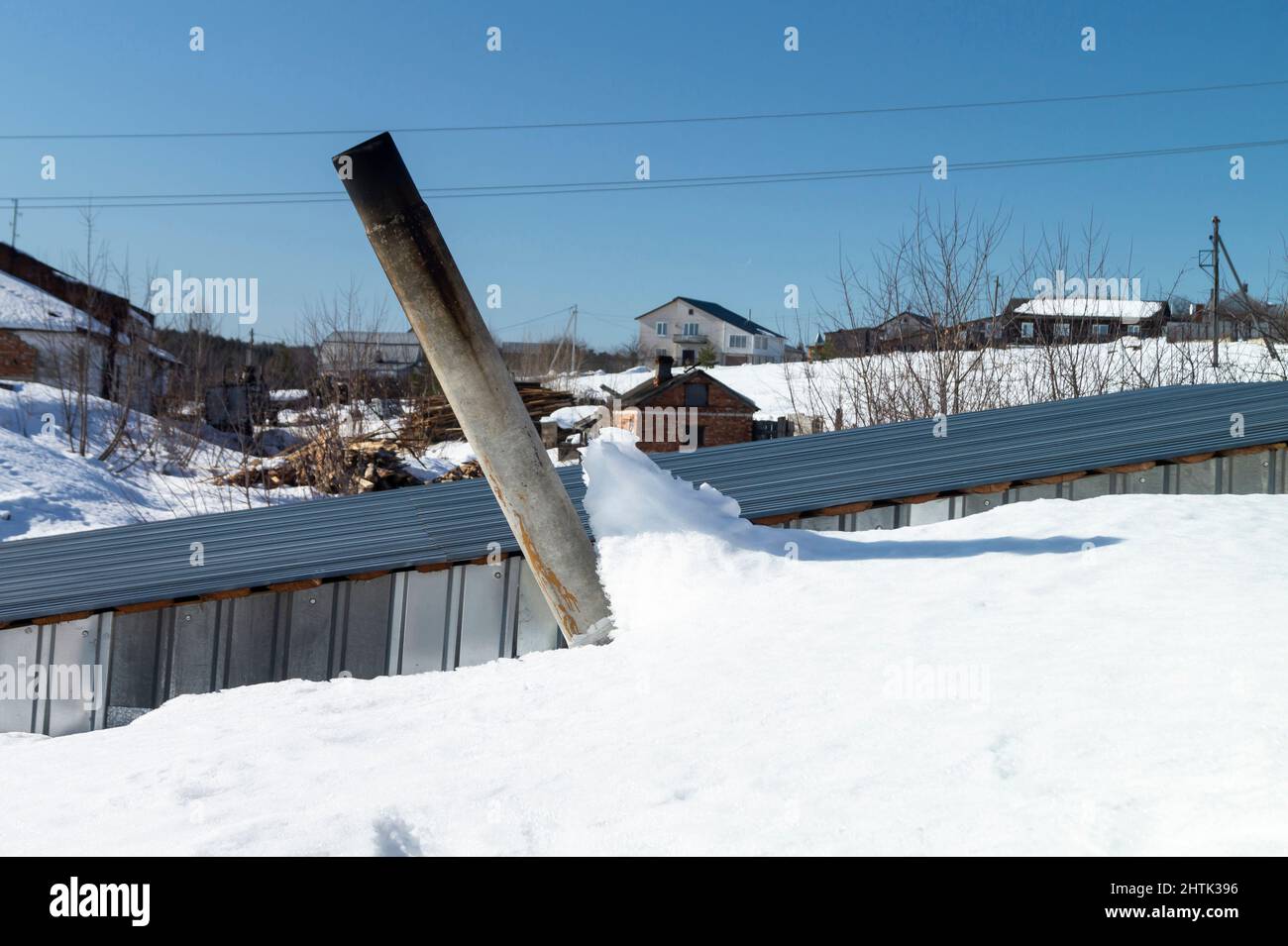 Beschädigter Schornstein auf dem Dach im Winter. Landschaft auf dem Land gegen den blauen Himmel Stockfoto