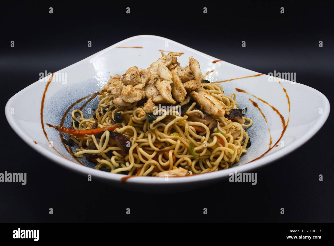 Gekochtes Huhn Yakisoba, asiatische Wok-Nudeln mit Huhn, Sesam, Teriyaki-Sauce und verzehrfertiges Gemüse. Studio Foto mit schwarzem Hintergrund. Stockfoto
