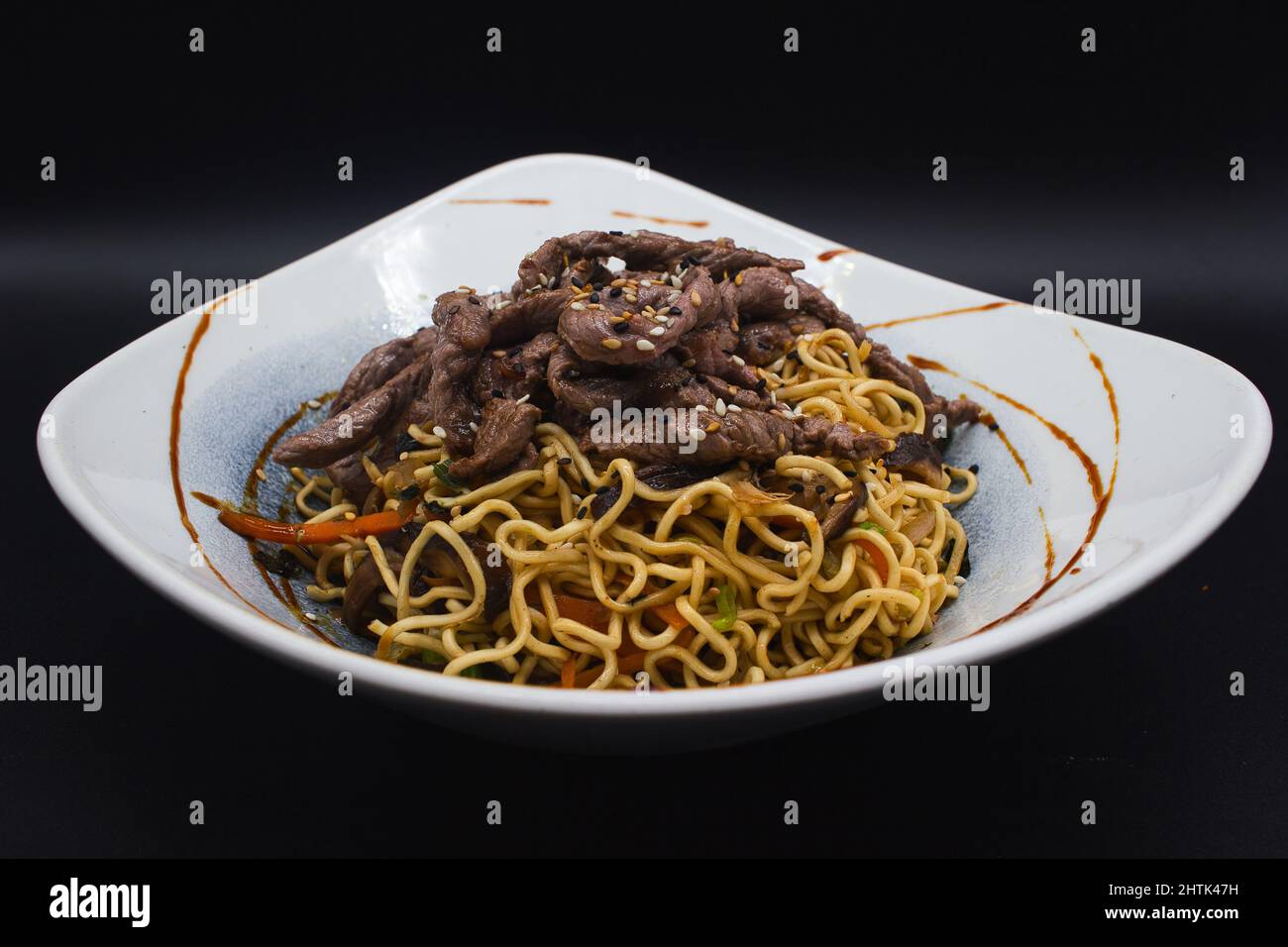 Gekochtes Rindfleisch Yakisoba, asiatische Wok-Nudeln mit Rindfleisch, Sesam, Teriyaki-Sauce und verzehrfertigem Gemüse. Professionelles Studio-Foto, schwarzer Hintergrund. Stockfoto